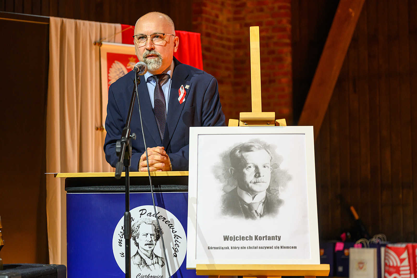 Dr Pleskaczyński podczas wykładu, z przodu portret bohatera konkursu